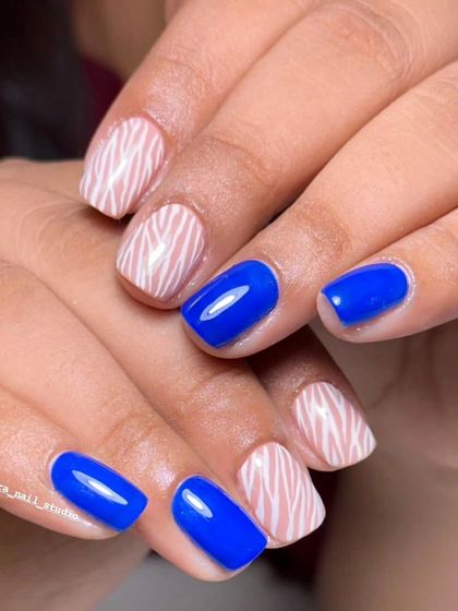 Bold and beautiful. A striking combination of vibrant solid blue nails and accent nails with a white zebra stripe pattern.