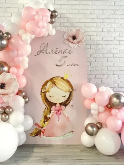 A charming princess-themed birthday setup. The arched backdrop features a sweet princess illustration, framed by an organic balloon garland in shades of pink, white, and chrome silver.