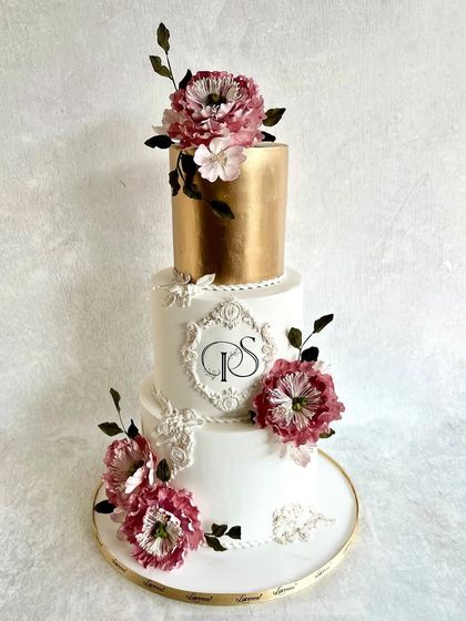 This wedding cake design is all about modern elegance. The top tier is finished in a brilliant edible gold, contrasting with the clean white tiers below. The cake is decorated with a custom monogram and large, handmade sugar peonies.