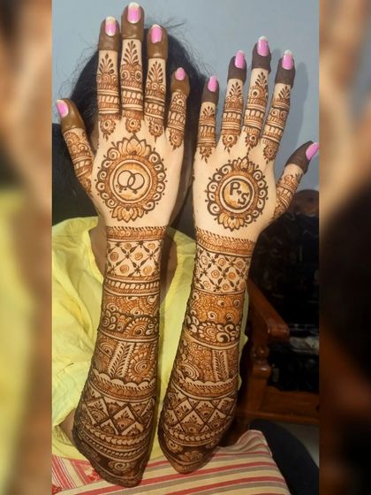 This bridal design includes personalized touches, with the couple's initials and wedding rings incorporated into the mandala on the palms. The rest of the arms feature classic bridal patterns.