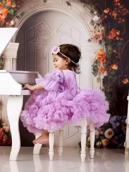 A little girl in a fluffy purple dress playing a miniature white piano, set against a magical floral backdrop.