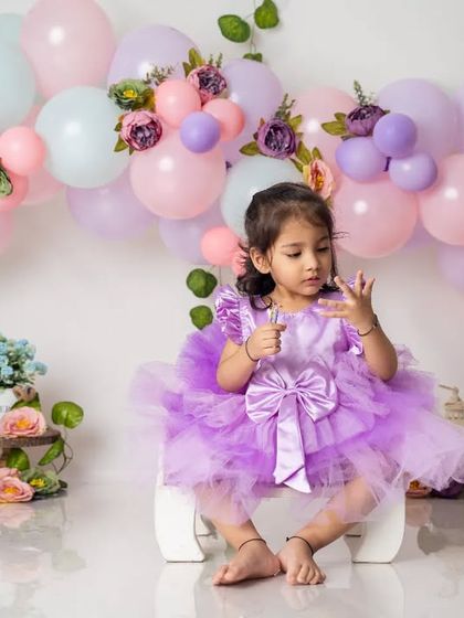 A thoughtful moment from a two-year-old birthday girl, dressed in a beautiful purple tutu against a backdrop of pastel balloons.