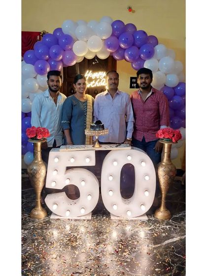 A happy family celebrating a 50th birthday milestone. We provided a simple purple and white balloon arch and large, bright light-up marquee numbers for the '50', creating the perfect backdrop for memorable family photos.