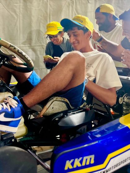 A young driver gets comfortable in his new KKM-liveried kart, surrounded by his supportive team.