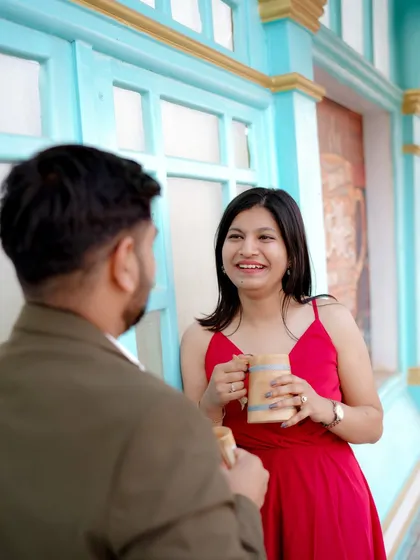 A playful moment sharing a drink against a vibrant blue door, reminiscent of a European street. The woman's bright red dress pops against the cool tones, creating a lively and stylish pre-wedding photo.