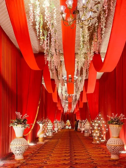 This entrance features a ceiling of hanging floral strings under red fabric drapes, adding a delicate and romantic touch to the walkway.