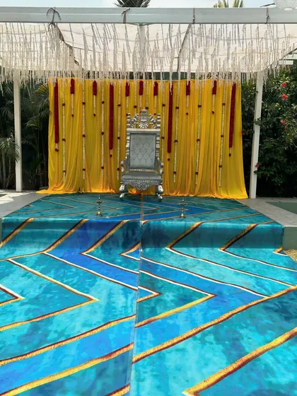 We create elegant and regal stage setups for important family ceremonies. This design features a beautiful silver throne against a bright yellow backdrop with delicate floral hangings, perfect for a naming ceremony or Dhoti function.