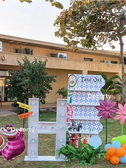A fun photo-op area at an Alice in Wonderland party, featuring the Cheshire Cat and a large marquee letter 'H'.