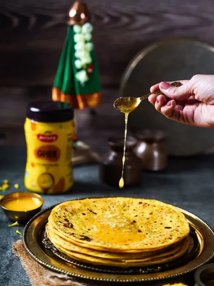 A stack of soft Puran Polis with a stream of ghee being poured over them. This shot, styled with a Gudi in the background, perfectly captures the essence of the Maharashtrian new year festival.