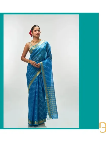 This ethereal Persian blue silk organza saree features delicate gold zari checks. The pallu is a beautiful interplay of geometric and floral motifs.