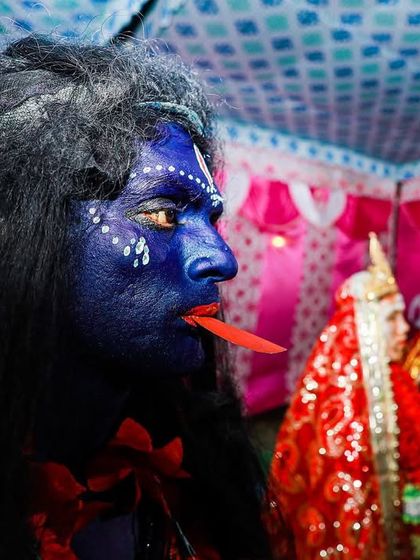 A performer with his face painted blue, representing a deity for the Gajan Festival, is captured in a moment of preparation.