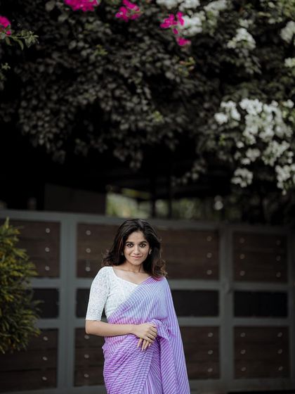 An elegant outdoor portrait of a model in a beautiful saree. The natural setting with blooming flowers adds a soft, romantic feel.