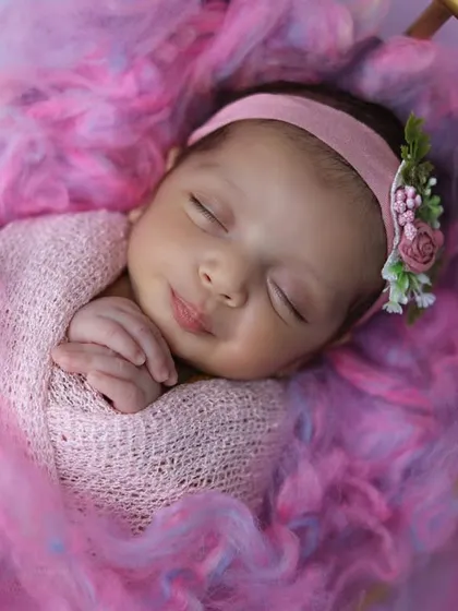 A serene portrait of a sleeping newborn, smiling sweetly while swaddled in soft pink fabrics. This image embodies the gentle, artistic approach I take to newborn photography, focusing on their peaceful innocence.