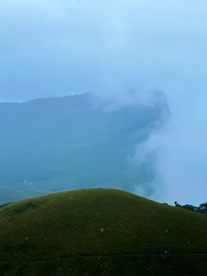 The misty peaks of Kudremukha partially hidden by clouds, creating a dramatic and beautiful landscape.