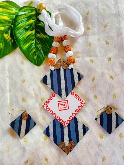 A geometric fabric necklace with striped patterns and a hand-painted centerpiece. The white threadwork provides a beautiful contrast against the blue fabric.