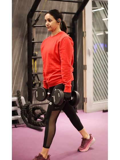 A member performs walking lunges with dumbbells, a dynamic exercise that builds leg strength and improves cardiovascular endurance.