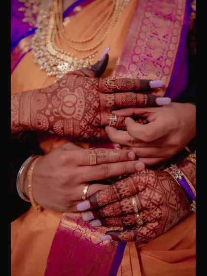A close up shot of the couple's hands, highlighting the rich stain of the bride's mehendi, which includes her wedding hashtag.