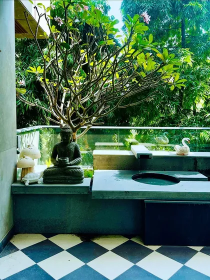 A stunning balcony water feature in Swami Nagar, Delhi. The design includes a gentle fountain, a Buddha statue for serenity, and a beautiful Frangipani tree, all set against a backdrop of lush greenery.