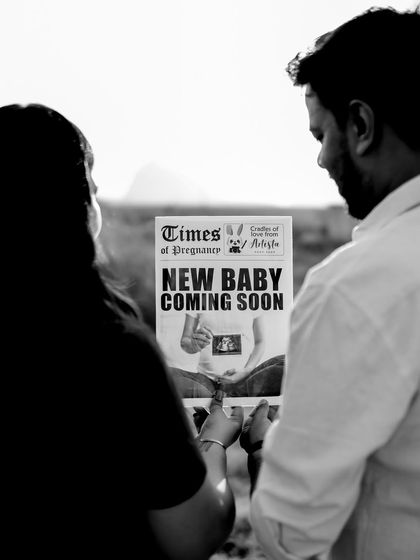 A black and white shot of the couple looking at their "New Baby Coming Soon" newspaper together, with the bright sky creating a high-contrast, hopeful image.