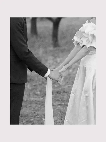 A close-up detail of them holding hands, the delicate fabric of her blindfold trailing between them. A simple, symbolic black and white image about their connection.