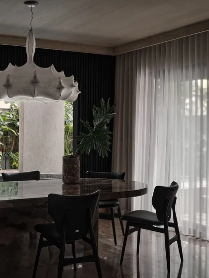 A close-up of the dining area, showing the contrast between the heavy marble table and the delicate, flowing sheer curtains. The space feels both grounded and light.