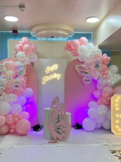 The full view of the pink butterfly-themed 6th birthday stage, showing the symmetrical balloon arrangements and the glowing marquee number.