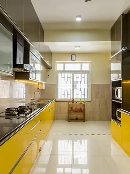 A bright and sunny parallel kitchen with glossy yellow cabinets that reflect light beautifully. The black countertop and stainless steel appliances provide a striking contrast, creating a modern and energetic atmosphere.