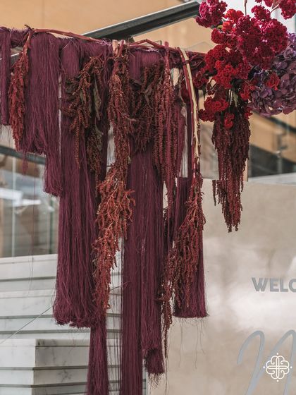 A detail of the fabric and floral installation at the entrance of the naming ceremony, featuring rich burgundy tones and varied textures.