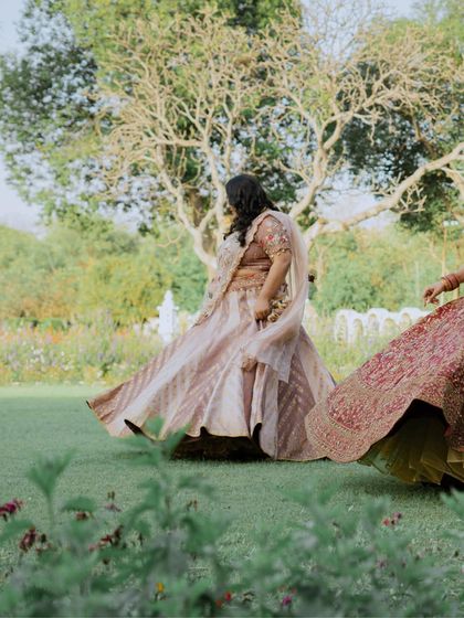 A fun, candid shot of the bride and her sisters twirling in their lehengas on the lawn.
