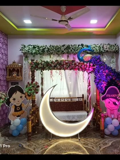 A baby shower decoration featuring a peacock made of flowers on a traditional swing. The lighted moon prop and character cutouts complete this elaborate home setup.