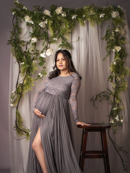 A full-length portrait showcasing a stunning grey lace and tulle gown. The floral vine backdrop adds a touch of natural elegance to this beautiful solo shot.