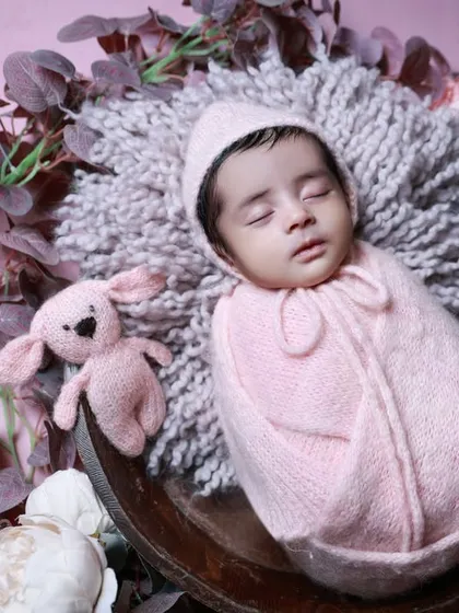 A close-up of the baby from the 'Dry Lagoon' session, showing her cozy pink outfit and matching teddy bear.