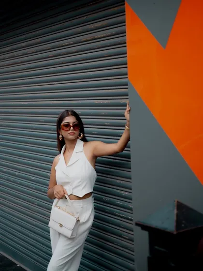A clean and modern street style shot. The model's all-white outfit stands out against the grey and orange background, creating a minimalist and chic look.