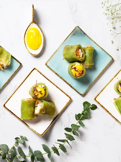 An overhead view of our elegantly plated appetizers. These bite-sized green rolls are meticulously arranged on artisanal plates, demonstrating our belief that food and design go hand in hand.