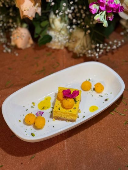 A modern take on a classic. This deconstructed cheesecake features a mango mousse, biscuit crumble, and motichoor-style pearls, garnished with an edible flower for a touch of elegance.