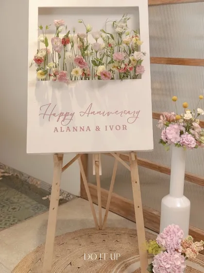A custom welcome sign for a special anniversary brunch. The easel holds a sign with a built-in shadow box filled with delicate wildflowers, perfectly capturing the event's romantic and artistic theme.