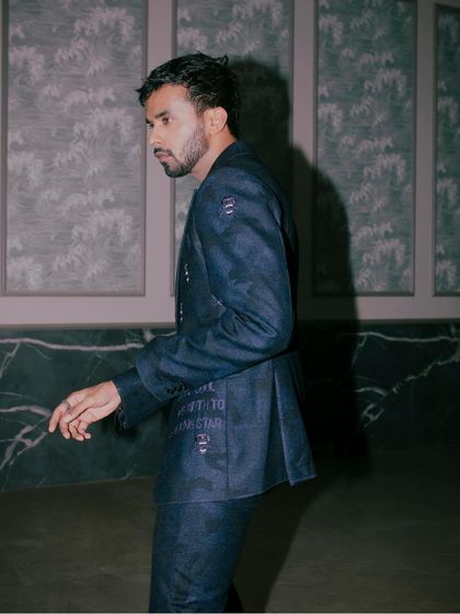 A side profile of Shakti Yadav in our dark blue suit, showing the subtle elegance and bold craftsmanship of the embroidered SGM logo motif.