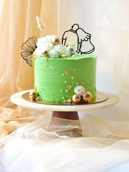An elegant anniversary cake with a fresh pineapple flavour. The light green buttercream is decorated with a modern couple topper, white flowers, and touches of gold.