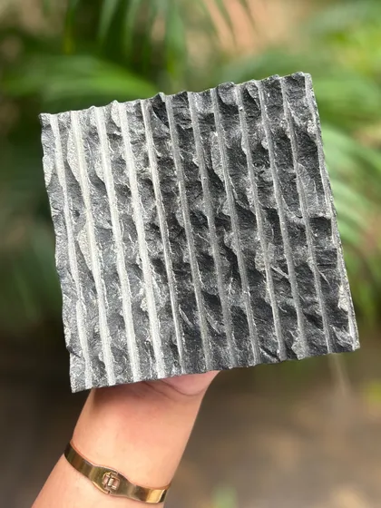 A hand-held sample of chiseled black stone, showcasing a rough, linear texture. This kind of tactile surface is perfect for creating dramatic accent walls or feature elements.