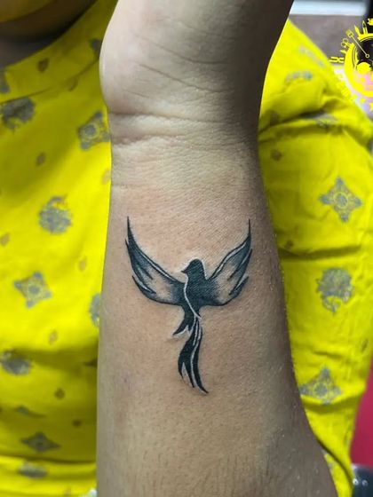 A small phoenix or bird tattoo on the wrist, symbolizing rebirth and freedom. The simple black shading gives it a classic look.