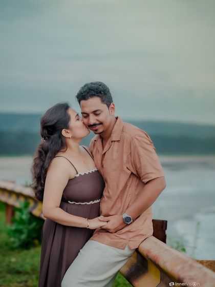 A sweet kiss on the cheek as the couple pauses on a roadside railing overlooking the water. This tender moment is a highlight of their romantic pre-wedding shoot.