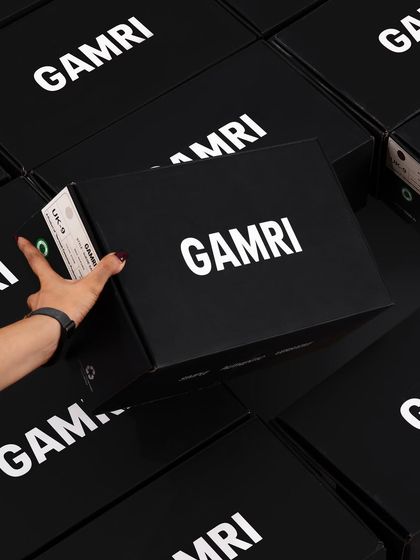 A shot focusing on the branding and packaging, with a hand selecting a Gamri shoebox from a large stack. This builds brand recognition.