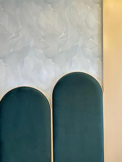 A close-up of the fine details in one of our bedroom designs. This image highlights the custom-arched headboard upholstered in rich green velvet with brass trim, set against a subtly patterned wall, showcasing our focus on texture and craftsmanship.