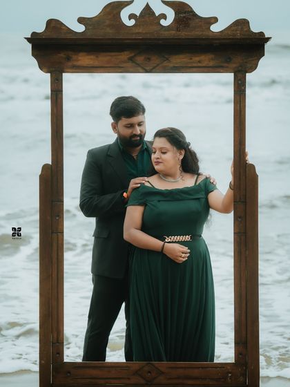 A creative pre-wedding shot using a wooden frame prop on the beach. The elegant green gown and the couple's pose create a picture-perfect moment.