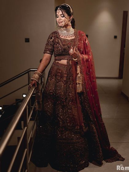 A full-length portrait of the bride on a staircase, her rich, dark lehenga and confident pose creating a powerful and elegant image.