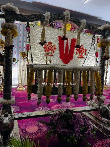 A beautifully decorated cradle for a naming ceremony. The setup features a backdrop of white flowers with a central 'Om' symbol, creating a serene and spiritual ambiance.