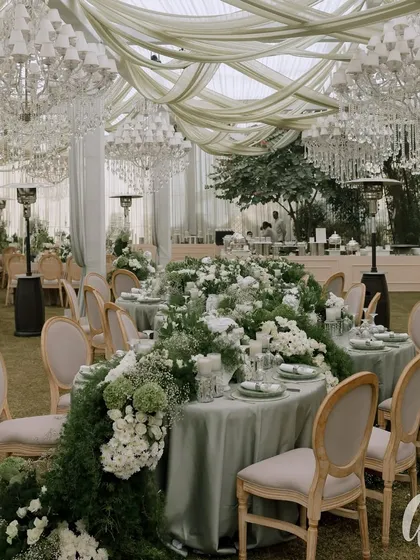 For this elegant reception, we designed a breathtaking tablescape featuring a lush floral runner cascading down the length of the table. Overhead, crystal chandeliers and soft drapery add a layer of romance and grandeur, creating a sophisticated dining experience under a custom-built marquee.