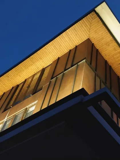 The corner of a building facade illuminated at dusk. This image captures the beauty of architecture shining under fading daylight, showcasing a perfect fusion of form, function, and material with expertly designed uplighting.
