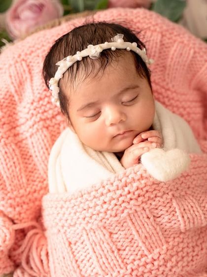 This peaceful portrait captures the baby swaddled and sleeping in a basket, surrounded by a wreath of delicate pink and cream roses.