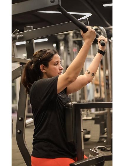 A member uses the lat pulldown machine, a key piece of equipment for developing back strength and a V-taper physique.